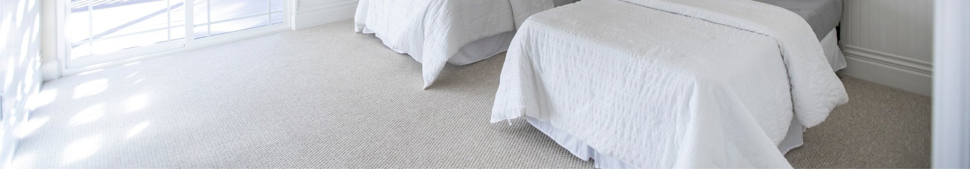 Two white beds in a bright bedroom with carpet floors